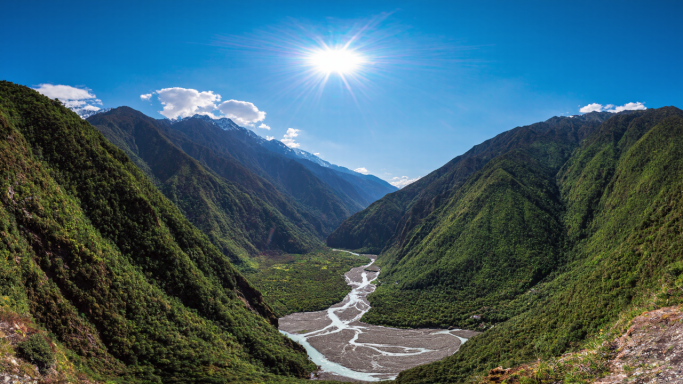 Panoramic view of a river winding through green mountains under a bright blue sky.